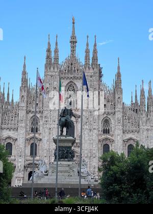 Vorderansicht der Mailänder Kathedrale mit Reiterstatue und Fahnen auf der Piazza del Duomo, Italien. Stockfoto