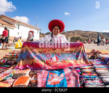 Andenfrau verkauft bunte traditionelle Textilien auf einem Kunsthandwerksmarkt in Cusco, Peru. Authentische indigene Kultur und lebendige handgefertigte Stoffe. Stockfoto