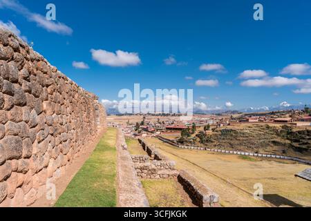 Alte Inka-Steinmauer in Chinchero, Cusco, Peru, mit Blick auf das Tal, das Dorf, und die schneebedeckten Anden unter blauem Himmel. Stockfoto