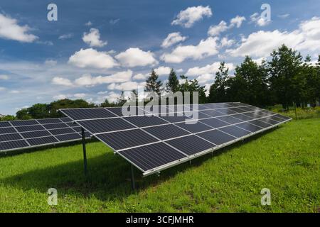 Reihen von Solarpaneelen sind in einem üppigen grünen Feld installiert, die das Sonnenlicht einfangen. Der hellblaue Himmel ist mit flauschigen weißen Wolken verziert, die eine se schaffen Stockfoto
