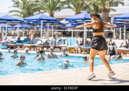 Eine junge weibliche Sportanimatorin macht Wassergymnastik für Menschen im Pool eines Hotelresorts. Stockfoto