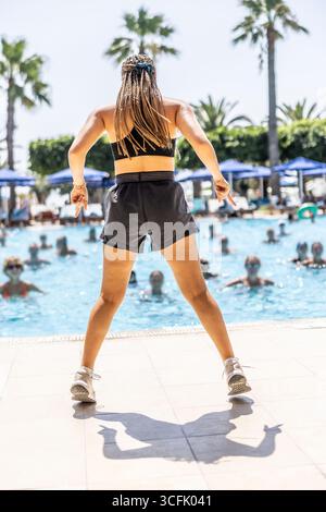 Eine junge weibliche Sportanimatorin macht Wassergymnastik für Menschen im Pool eines Hotelresorts. Stockfoto