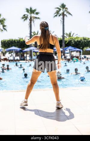 Eine junge weibliche Sportanimatorin macht Wassergymnastik für Menschen im Pool eines Hotelresorts. Stockfoto