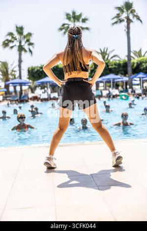 Eine junge weibliche Sportanimatorin macht Wassergymnastik für Menschen im Pool eines Hotelresorts. Stockfoto