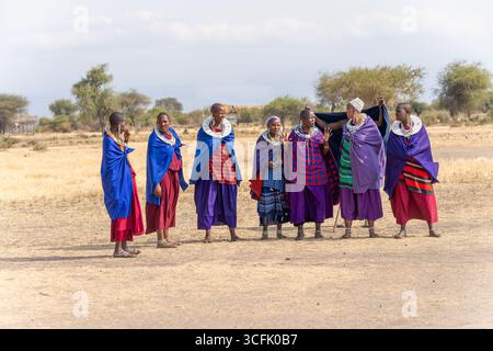 Maasai-Frauen, die in der Nähe ihres Dorfes im ländlichen Tansania einen traditionellen Tanz aufführen, zeigen lebendige kulturelle Kleidung und zeremonielle Bewegungen Stockfoto