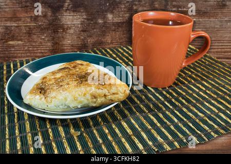 Eine knusprige und würzige Samosa in indischer Dreiecksform und eine Tasse Tee auf der braunen Holzmatte. Stockfoto