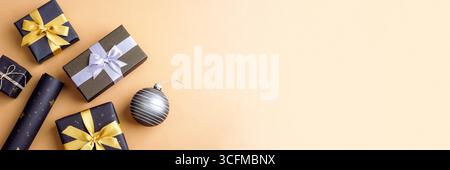 Elegante Geschenkboxen mit goldenen und silbernen Bändern und glänzender weihnachtskugel auf beigefarbenem Hintergrund. Festliche minimale Urlaubskomposition. Draufsicht, flache La Stockfoto