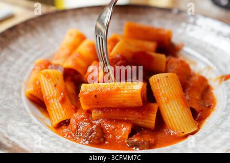 Ein junger Reisender, der Rigatoni Amatriciana (Rigatoni all’ Amatriciana) isst, traditionelle römische Pasta Stockfoto