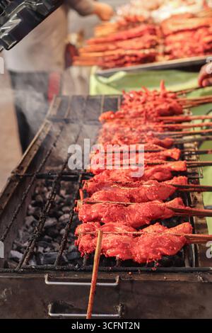 Straßenverkäufer grillen marinierte Hühnchenrippchen auf einem rauchigen Holzkohlegrill, rote Glasur und traditionelles asiatisches Straßenessen auf einem lebhaften Markt. Stockfoto