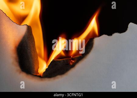 Weißes Papier brennt auf schwarzem Hintergrund, Nahaufnahme. Papier verbrennt, raucht und verwandelt sich in Asche. Feuer und Papier Stockfoto