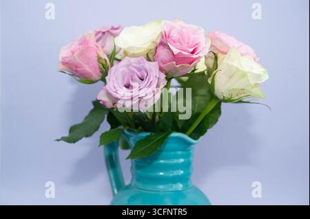 Strauß von bunten Rosen in türkisfarbener Keramikvase vor hellviolettem Hintergrund Stockfoto