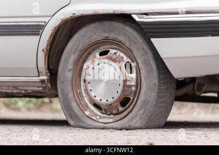 Ein Platten Reifen eines Autos aus der Nähe. Reparatur eines Platten Reifens an einem silbernen Auto, während er nachmittags auf einer Schotterstraße in der Nähe eines Reifenservice geparkt wurde Stockfoto