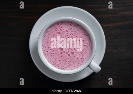 Rosa Matcha Latte mit Milch in weißer Tasse auf hölzernem Hintergrund, Nahaufnahme, Draufsicht. Trendiges Getränkekonzept Stockfoto