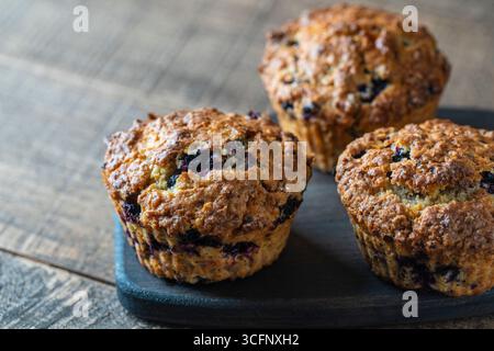 Köstliche Muffins mit Blaubeeren auf einem Holztisch, Nahaufnahme. Süßes Gebäck auf dem Brett. Frische Cupcakes zum Frühstück Stockfoto