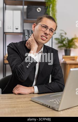 Kaukasischer Geschäftsmann freiberuflicher Kerl, der am Laptop arbeitet, am Schreibtisch sitzt Nackenschmerzen spürt, leidet an Wirbelsäulenverletzungen, unbequeme Haltung fühlt Müdigkeit und Überlastung am Arbeitsplatz Büro zu Hause. Stockfoto