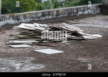 Stapel von entsorgten, verwitterten Bodenfliesen und Bruchstücken auf einer kiesigen Dachbetonoberfläche. Stockfoto