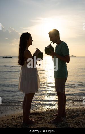 Touristen genießen erfrischendes Kokoswasser an einem wunderschönen Strand während eines lebhaften Sonnenuntergangs Stockfoto