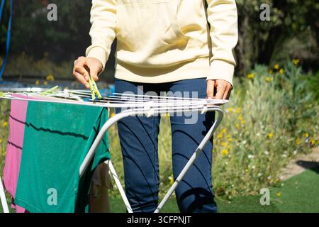 Frau hängt Wäsche an einer Wäscheleine in einem Garten und erledigt Haushaltsarbeiten an einem sonnigen Tag Stockfoto