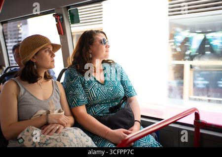 Zwei weibliche Touristen, die eine Besichtigungstour genießen und aus dem Busfenster auf die Stadtlandschaft blicken Stockfoto