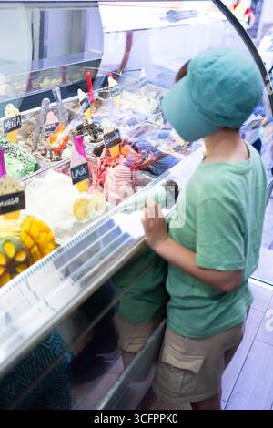 Kind, das Eis aus dem farbenfrohen Kühlschrank in der Eisdiele wählt Stockfoto
