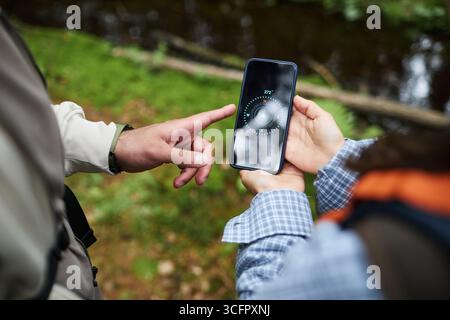 Kaukasischer junger erwachsener Mann und kaukasische junge erwachsene Frau mit Smartphone-Kompass-App im Freien, Mann zeigt auf den Telefonbildschirm, während er zusammen im Wald steht Stockfoto