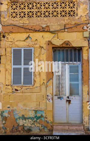 Verwitterte gelbe Wand mit abblätternder Farbe und verschließbaren Fenstern Stockfoto