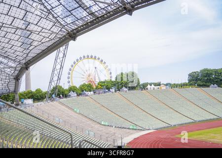 Offenes Stadion mit Blick auf ein Riesenrad im Hintergrund und grüne Sitzreihen, Olympiapark, München, Deutschland Stockfoto