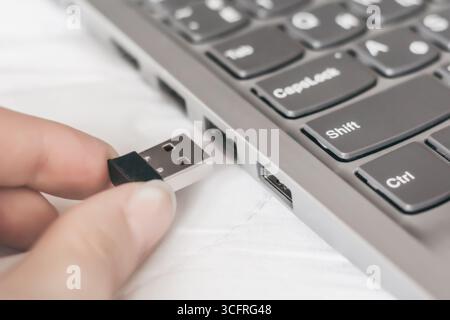 Famele Hand fügt den Empfänger des Universaladapters in den usb-Anschluss des Laptops ein Stockfoto