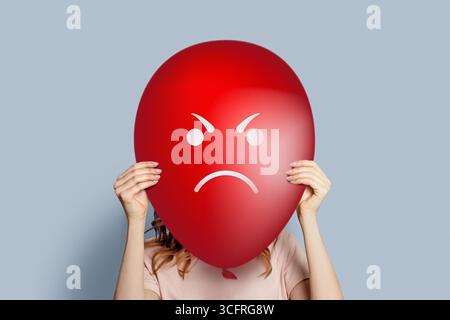 Mädchen, das Ballon hält, mit wütendem Gesicht isoliert über grauem Hintergrund. Wut- und Ärgerniskonzept Stockfoto