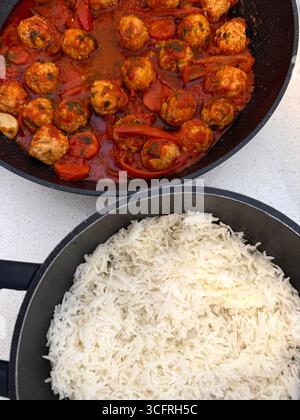In der Pfanne werden kochende Fleischbällchen in einer reichhaltigen Tomatensauce aufbewahrt, umgeben von bunten Paprika. Ein Topf zeigt flauschigen weißen Reis, der zum Beigeben bereit ist. Stockfoto
