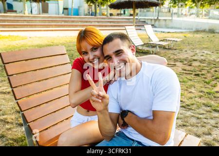 Glückliches Paar, das auf der Bank sitzt und ein Friedenszeichen drückt Stockfoto