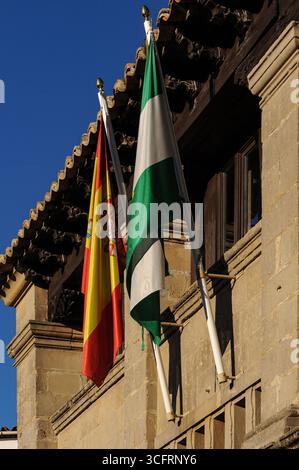 Rot, gelb, grün und weiß: Die Flaggen Andalusiens oder Andalusiens und der UNESCO-Weltkulturerbe-Stadt Baeza hängen an einem heißen Nachmittag im Antigua Carnicería-Gerichtsgebäude aus der Frührenaissance, einem ehemaligen Schlachthof und Metzgerei auf der Plaza del Pópulo, schlafend zusammen. Stockfoto
