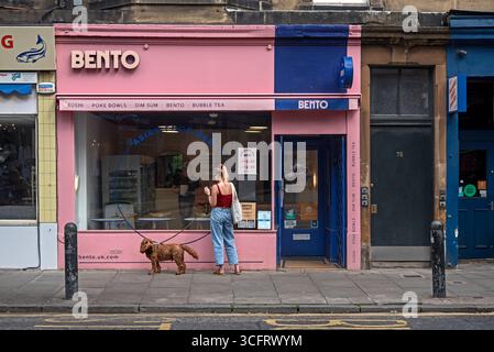 Junge Frau und Hund stehen vor der Bento Asian Food Bar in Raeburn Place, Stockbridge, Edinburgh, Schottland, UK. Stockfoto