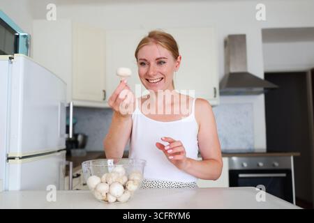 Lächelnde Frau, die frische Pilze in der modernen Küche zubereitet Stockfoto