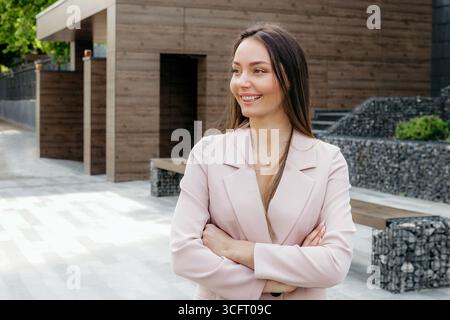 Eine kaukasische Marketerin in einem Anzug faltete ihre Hände und lächelte, während sie vor dem Hintergrund eines Bürogebäudes auf der Straße stand. Kopierbereich Stockfoto