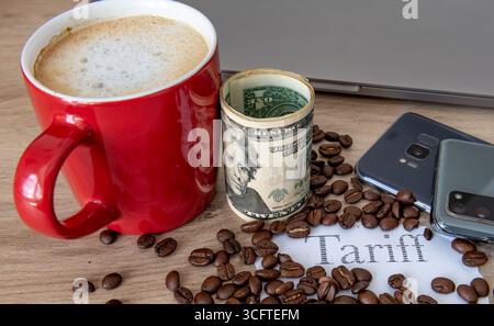 Eine Tasse Kaffee, Kaffeebohnen, eine Rolle US-Dollar-Scheine, das gedruckte Wort „Tarif“ und elektronische Waren auf einem Tisch. Ein US-Zollsteuerkonzept. Stockfoto