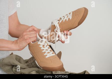 Frau, die braune Turnschuhe in der Hand hält, während sie nach dem Online-Shopping zu Hause den Lieferkarton auspackt. Weibliche Kundin öffnet das Paket mit neuer Kleidung Stockfoto