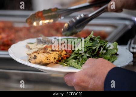 Gäste des Hochzeitsempfangs haben einen Teller vom Buffet mit Hühnchen und Salat zum Essen. Stockfoto