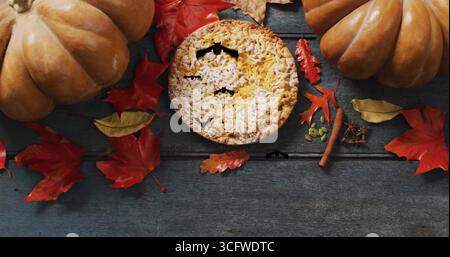 Kürbiskuchen und Herbstblätter mit herabfallenden Blättern auf hölzernem Hintergrund Stockfoto