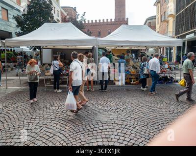 Cremona, Italien - 23. August 2025 geschäftige Outdoor-Marktszene unter weißen Zelten auf dem Kopfsteinpflasterplatz in Cremona, Italien, mit verschiedenen Käufern und Stockfoto