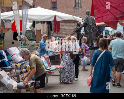 Cremona, Italien - 23. August 2025 geschäftige Outdoor-Marktszene in Norditalien mit verschiedenen Käufern, die bunte Textilien und lokale Produ durchsuchen Stockfoto