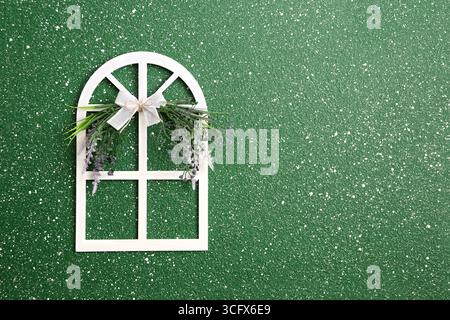 Kleines dekoratives Holzfenster mit Spitzenschleife und Blume auf grüner Stuckwand. Süßer Home-Style-Hintergrund. Bezauberndes Holzfenster mit lac Stockfoto