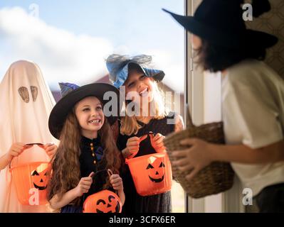 Glückliche Leute feiern Halloween. Erwachsene behandelt Kinder im Freien mit Süßigkeiten. Stockfoto
