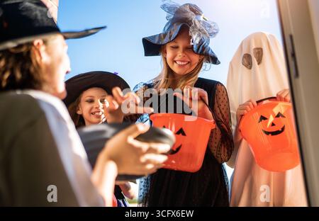 Glückliche Leute feiern Halloween. Erwachsene behandelt Kinder im Freien mit Süßigkeiten. Stockfoto