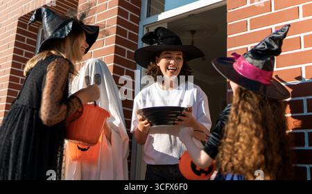 Glückliche Leute feiern Halloween. Erwachsene behandelt Kinder im Freien mit Süßigkeiten. Stockfoto