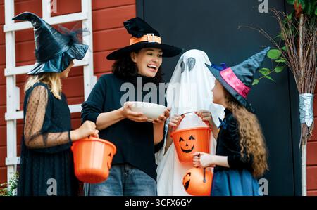 Glückliche Leute feiern Halloween. Erwachsene behandelt Kinder im Freien mit Süßigkeiten. Stockfoto