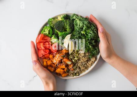 Die Hände einer Frau halten eine vegane buddha-Schüssel mit frischem Gemüse und Quinoa Stockfoto