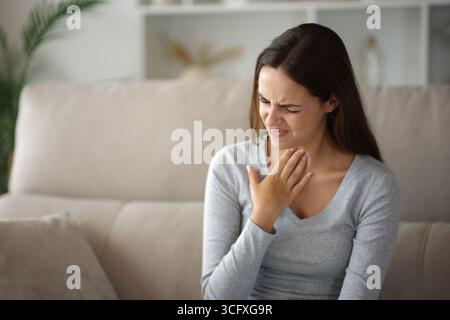 Frau mit Halsschmerzen, die sich zu Hause auf einer Couch beschwert Stockfoto