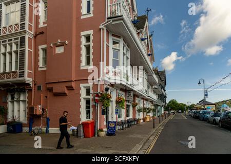 Kellner mit Smartphone auf dem Gehweg vor einem Gebäude mit hängenden Körben mit Blumen in Dartmouth, Devon, England, Großbritannien Stockfoto