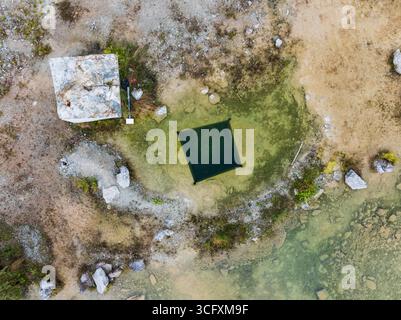 Von oben aus betrachtet ein mysteriöses tiefes quadratisches Loch, das in das klare türkisfarbene Wasser eines überfluteten Steinbruchs getaucht ist. Stockfoto